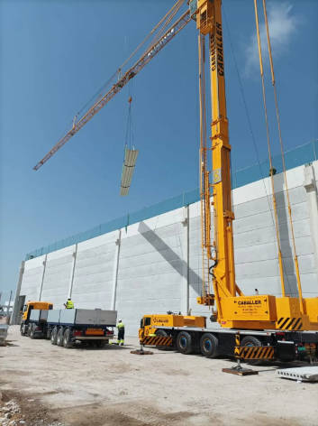 Grúa torre móvil autopropulsada elevando paneles de construcción por encima de un edificio industrial de Zaragoza